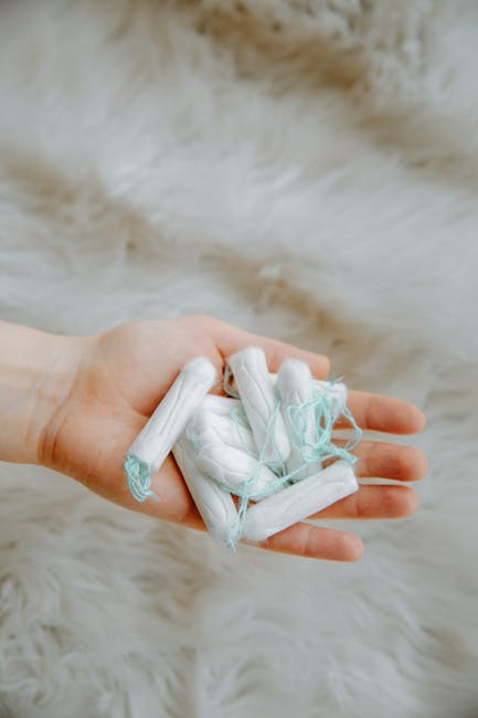 A person's hand holding a small pile of used disposable sanitary pads and tissues, with some of the pads wrapped in white and light blue plastic packaging, against a soft, cream-colored furry background. The image relates to waste disposal or personal hygiene care, which could be part of the packing and loading process during a home relocation or move. Man with Van Welling offers removals services that include the safe disposal of household waste, such as these items, during house moves or furniture transport. The scene highlights the importance of proper waste management and packing hygiene when preparing for a move, ensuring a clean and organized space inside the property or on the loading area outside.